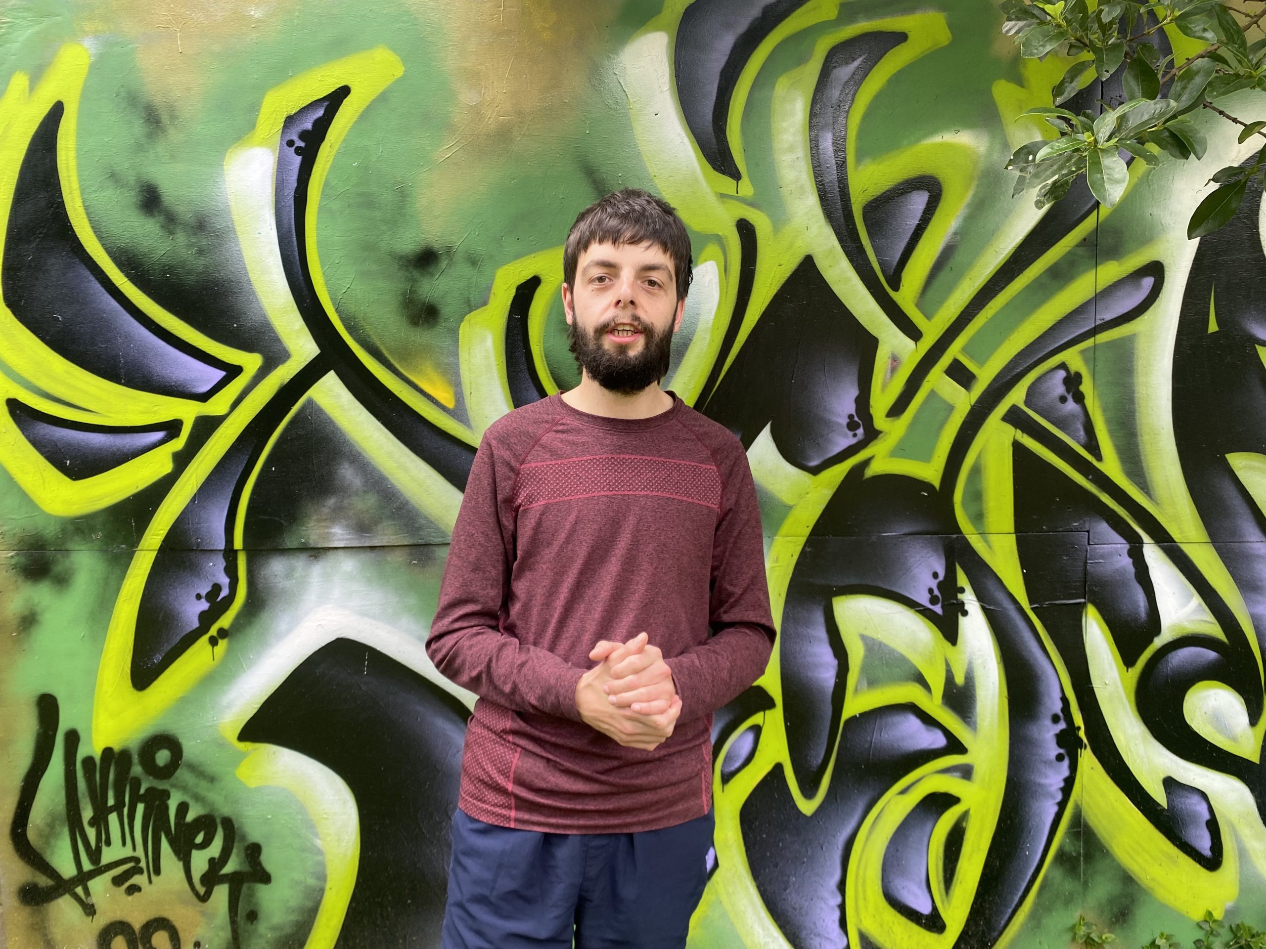 Oliver standing with his hands clasped in front of a graffiti wall