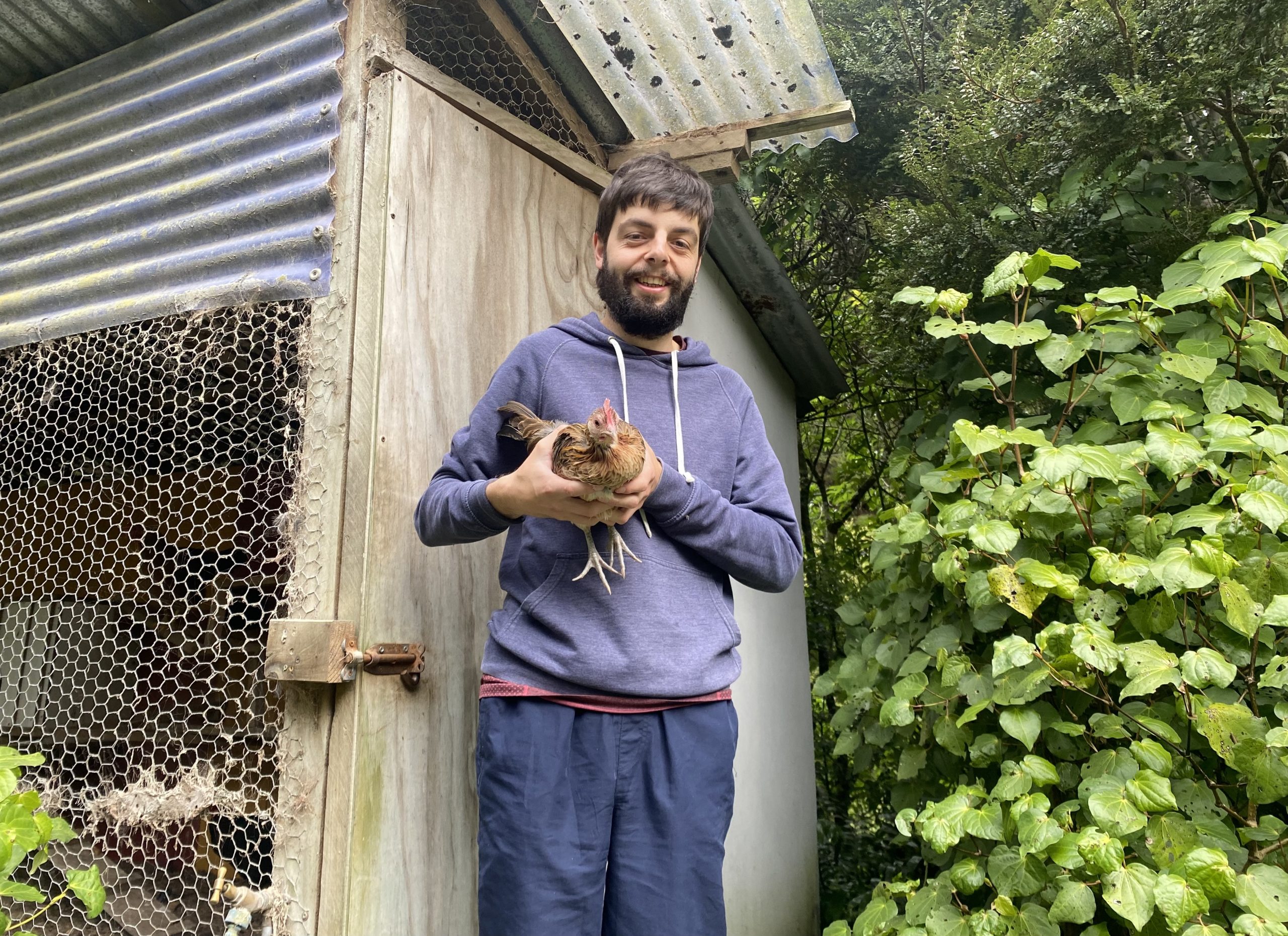 Oliver holding a chicken in his arms outside of his chicken pen